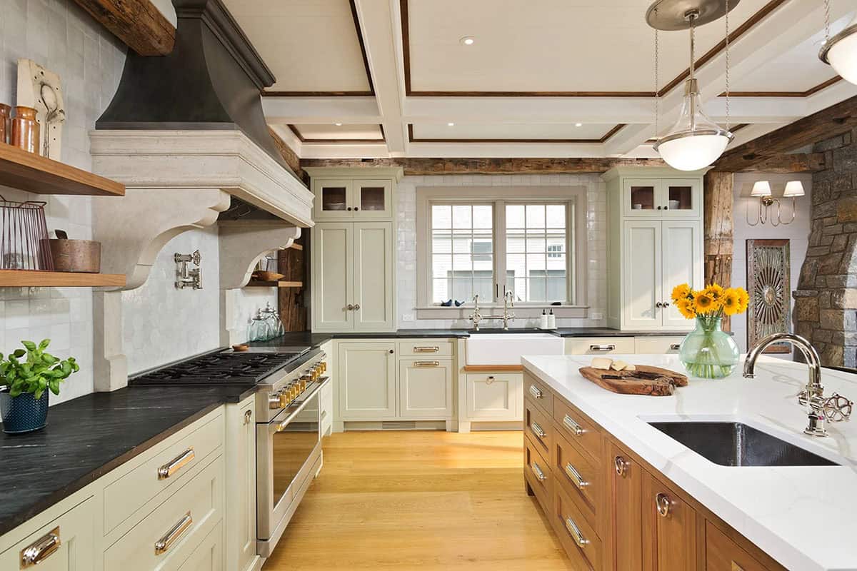 Farmhouse kitchen showing soapstone perimeter counters, sage cabinetry, stone hood, and walnut island with white marble top