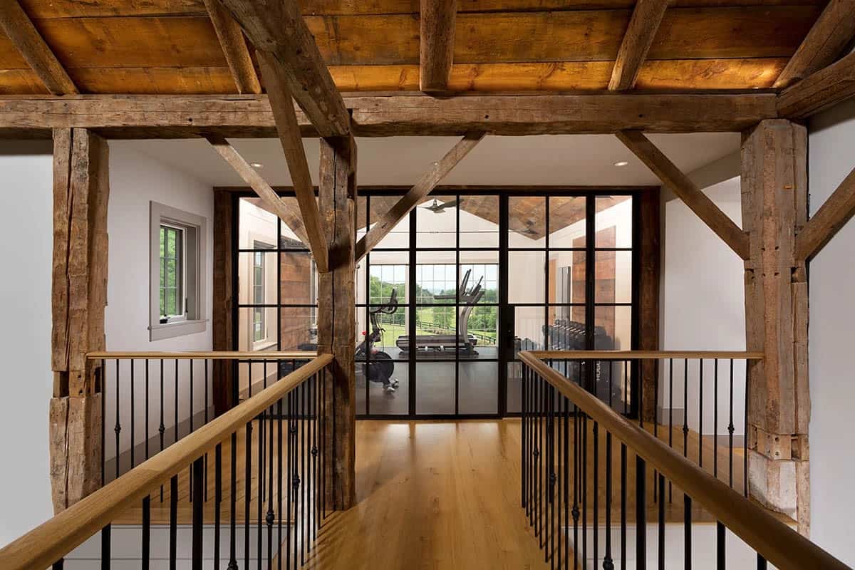 Upper hallway of restored barn with original timber frame, oak railings, and steel-framed gym beyond