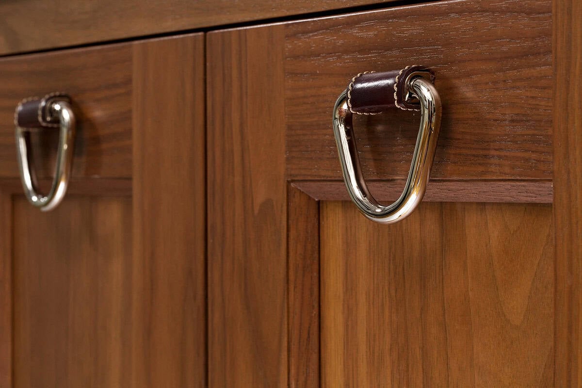 Close-up of walnut cabinet drawer with polished nickel and leather D-ring pull hardware detail