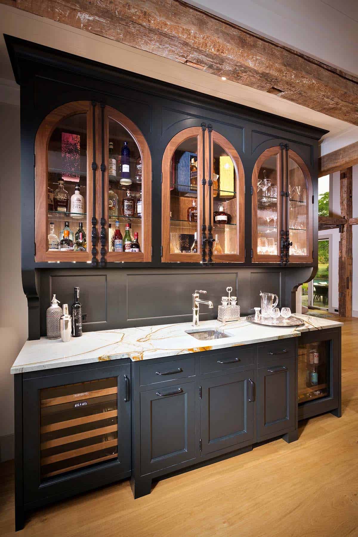 Built-in home bar with dark cabinetry, arched walnut glass doors, gold-veined marble countertop, and wine fridge
