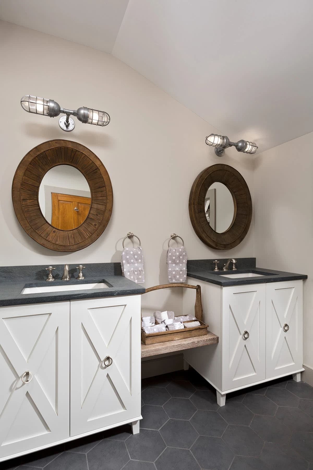 Kids bathroom with dual white vanities, soapstone countertops, round wood mirrors, and industrial wall sconces