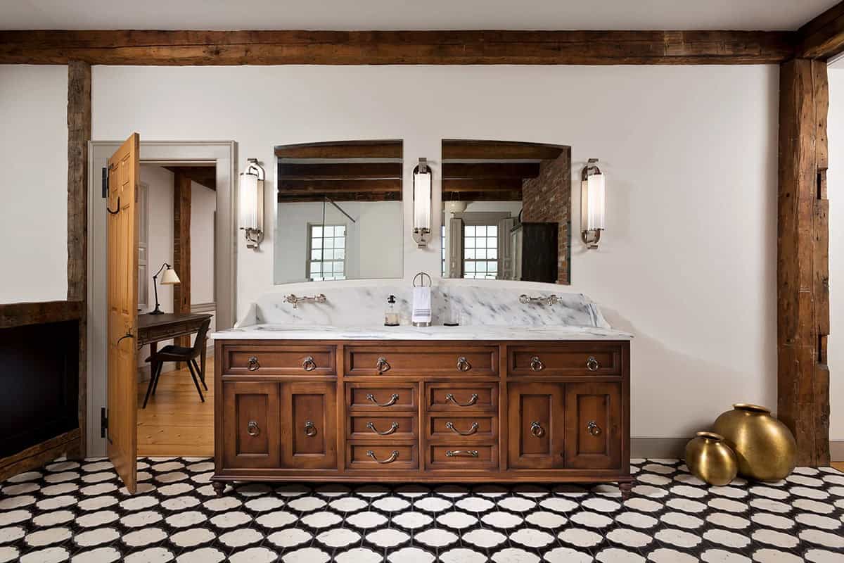 Primary bathroom vanity with walnut double vanity, marble countertop, black and white patterned tile floor, and exposed timber beams