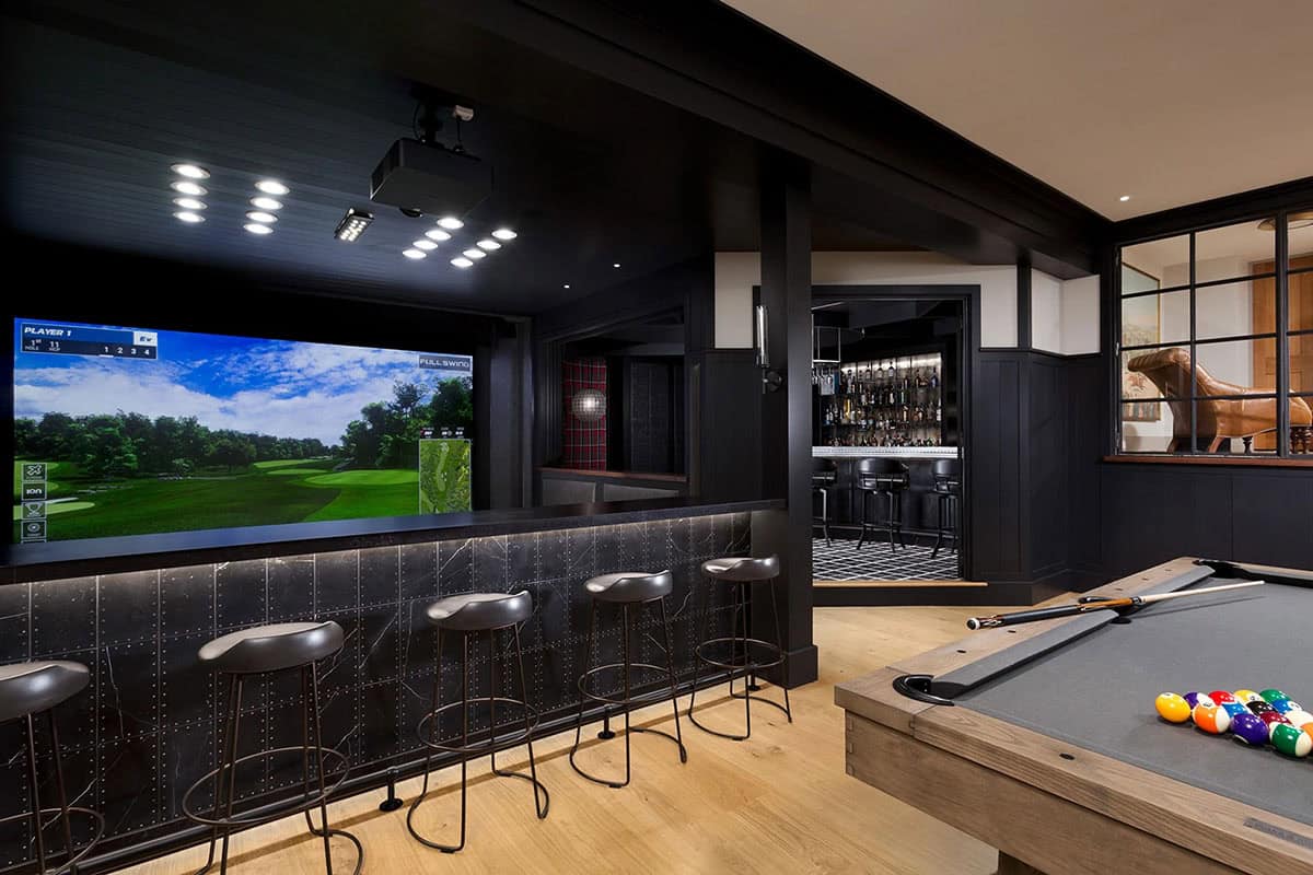 Lower level entertainment room with golf simulator, pool table, bar seating, and adjacent speakeasy bar