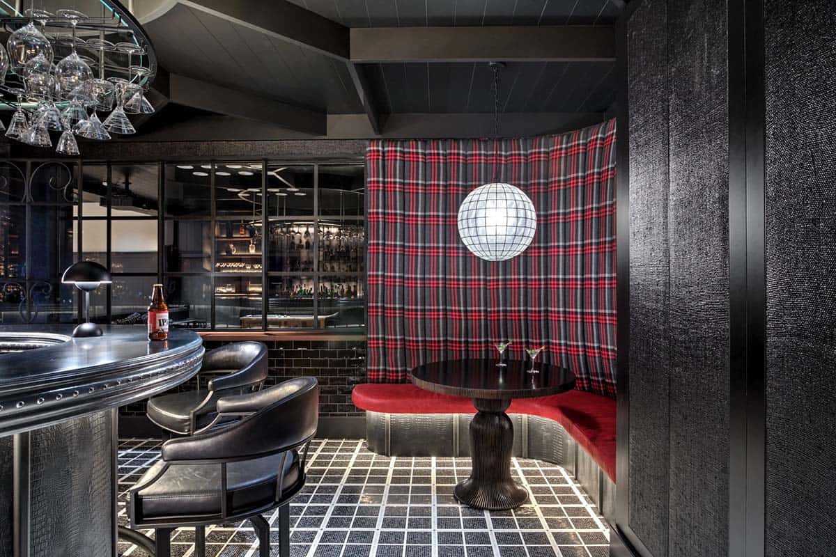 Moody speakeasy bar with tartan booth seating, disco ball pendant, black tile floor, and mirrored bar behind