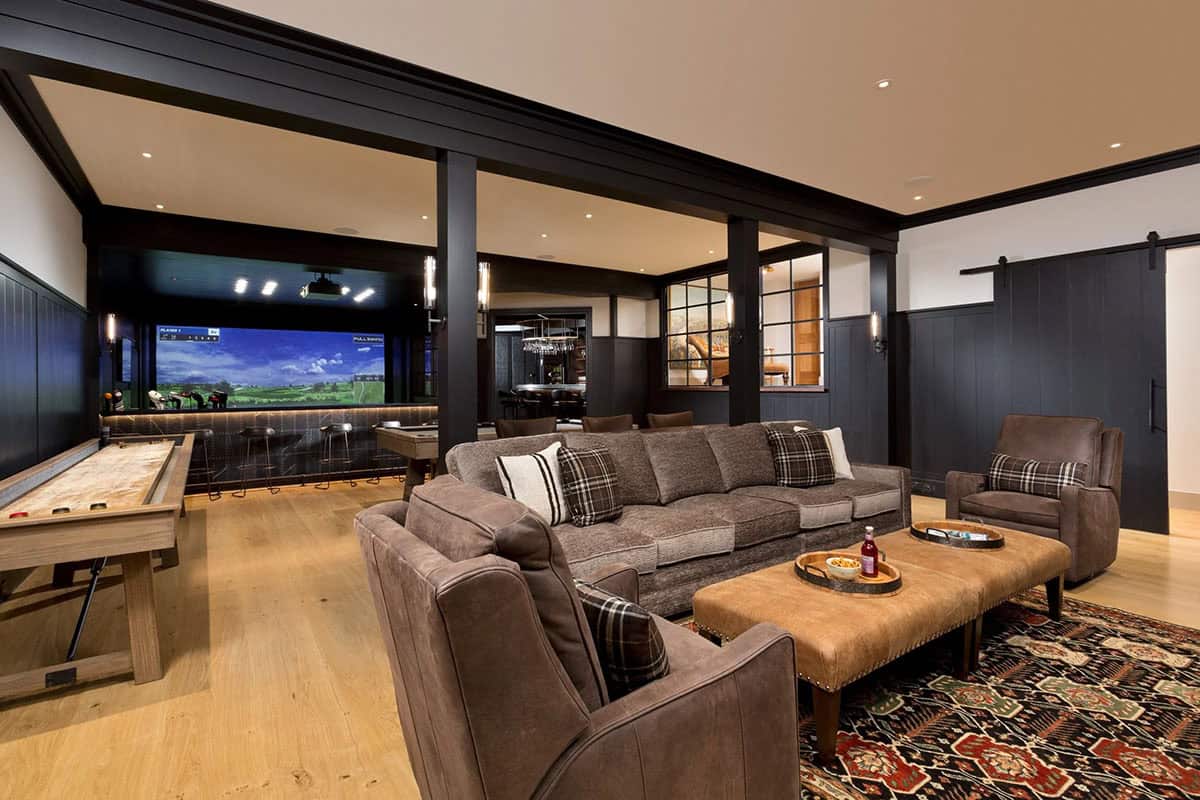 Lower level game room with shuffleboard, leather sofas, golf simulator screen, and barn door details