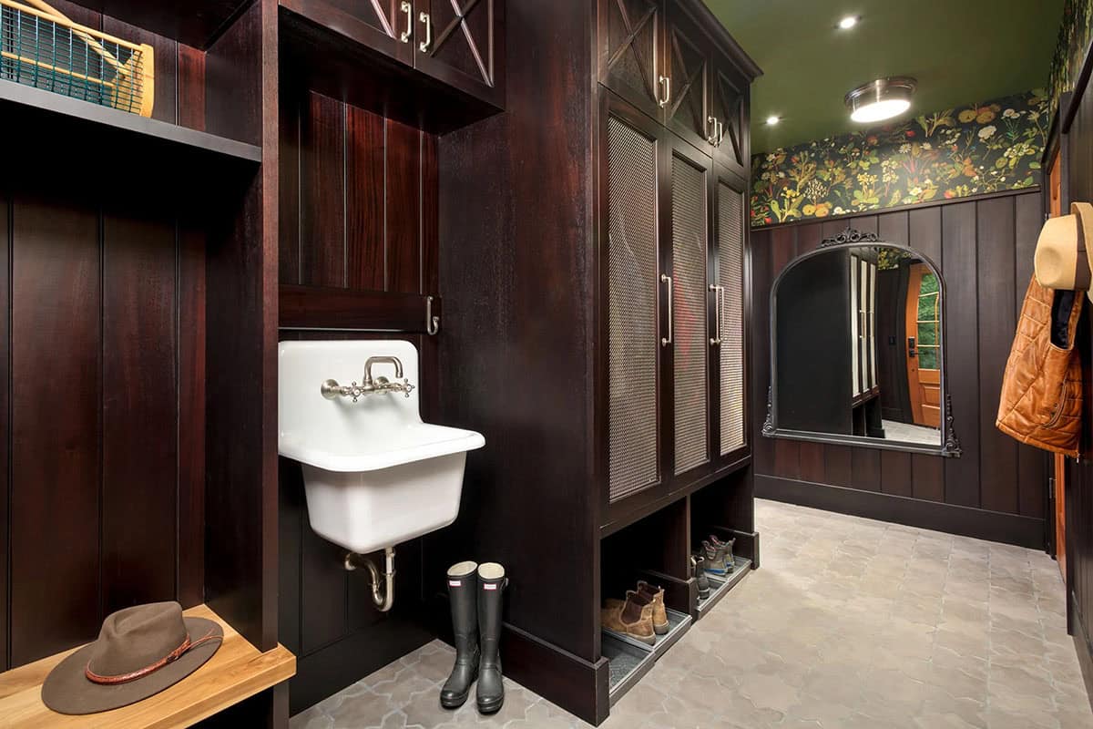 Mudroom with dark stained wood lockers, cast iron utility sink, botanical wallpaper, and patterned tile floor