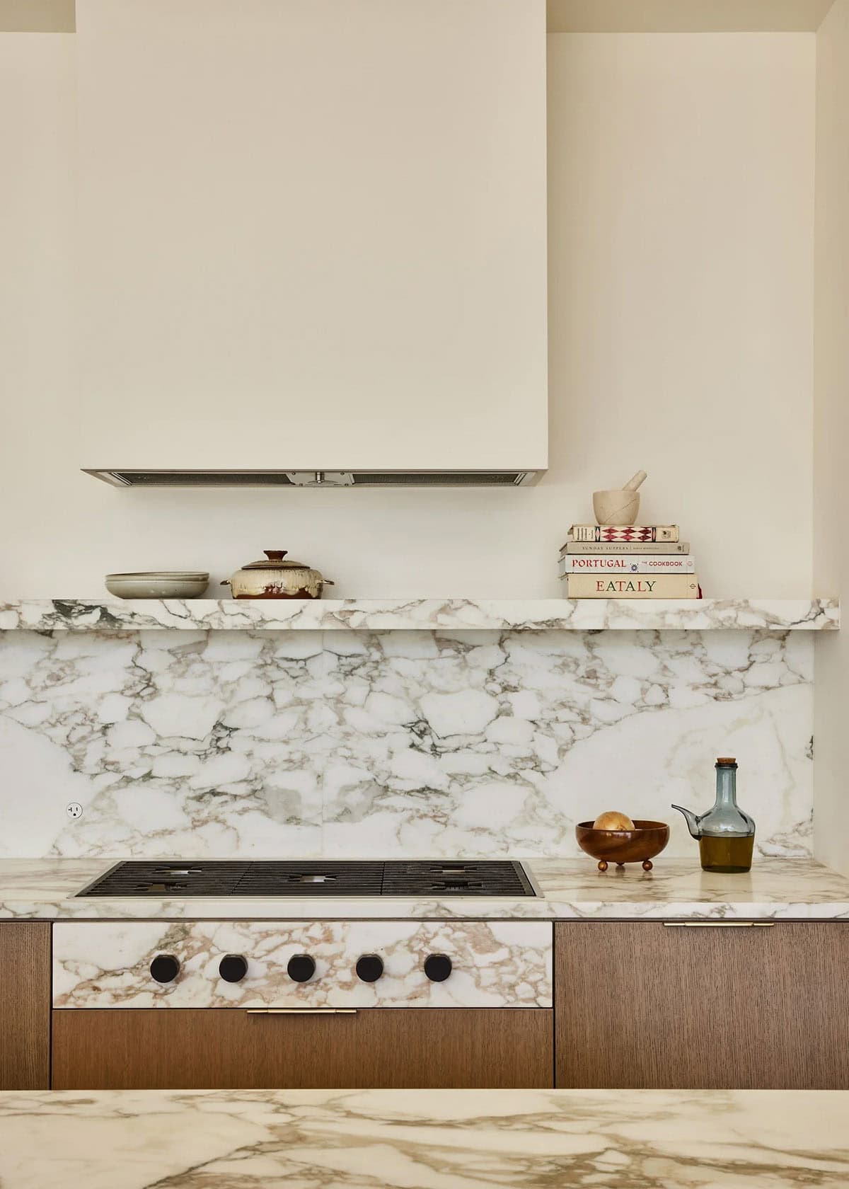 Kitchen cooktop with dramatic veined marble backsplash, slab shelf, plaster range hood, and walnut cabinetry