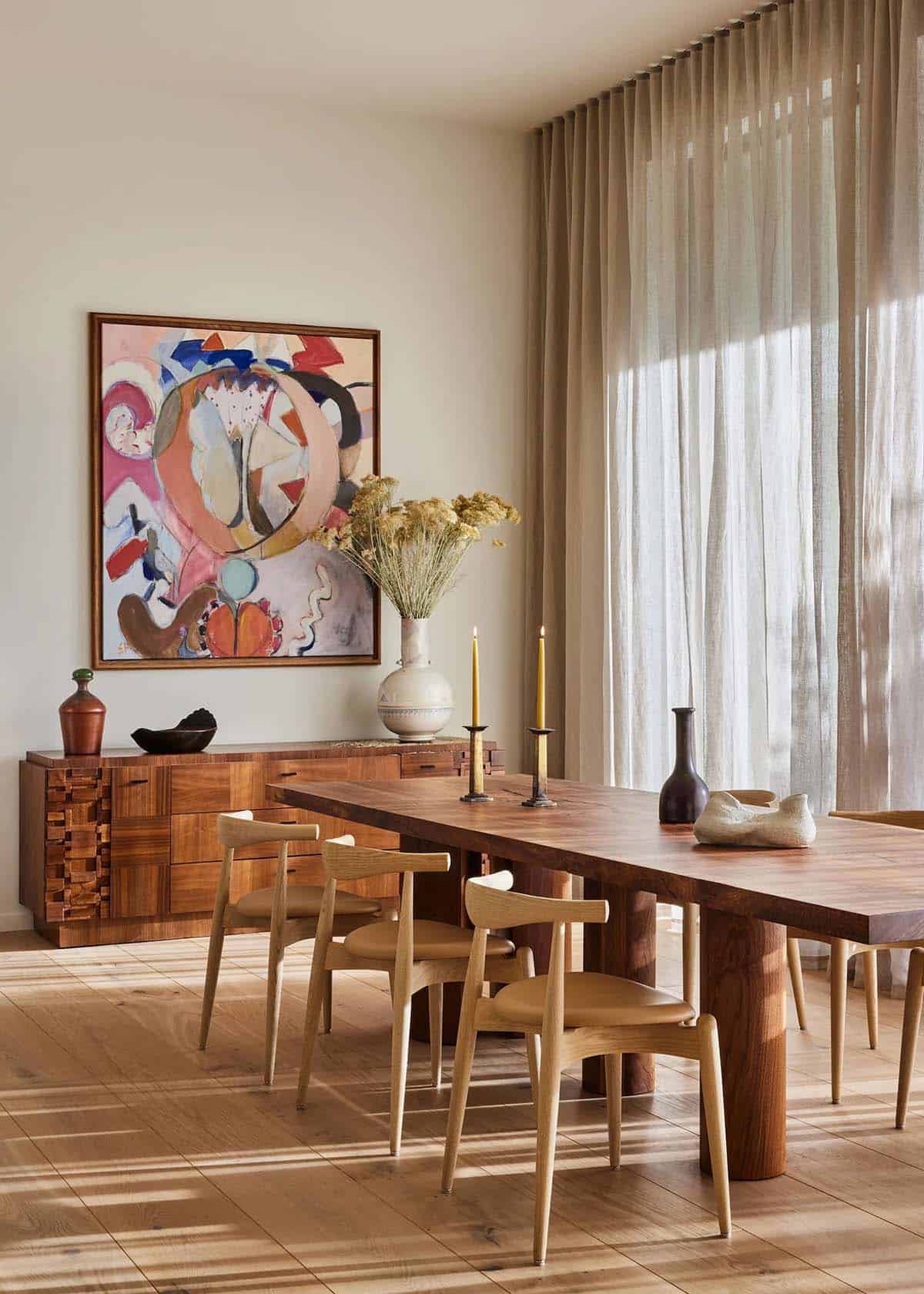Dining area detail showing walnut dining table with candles and dried florals, abstract artwork, and carved wooden sideboard