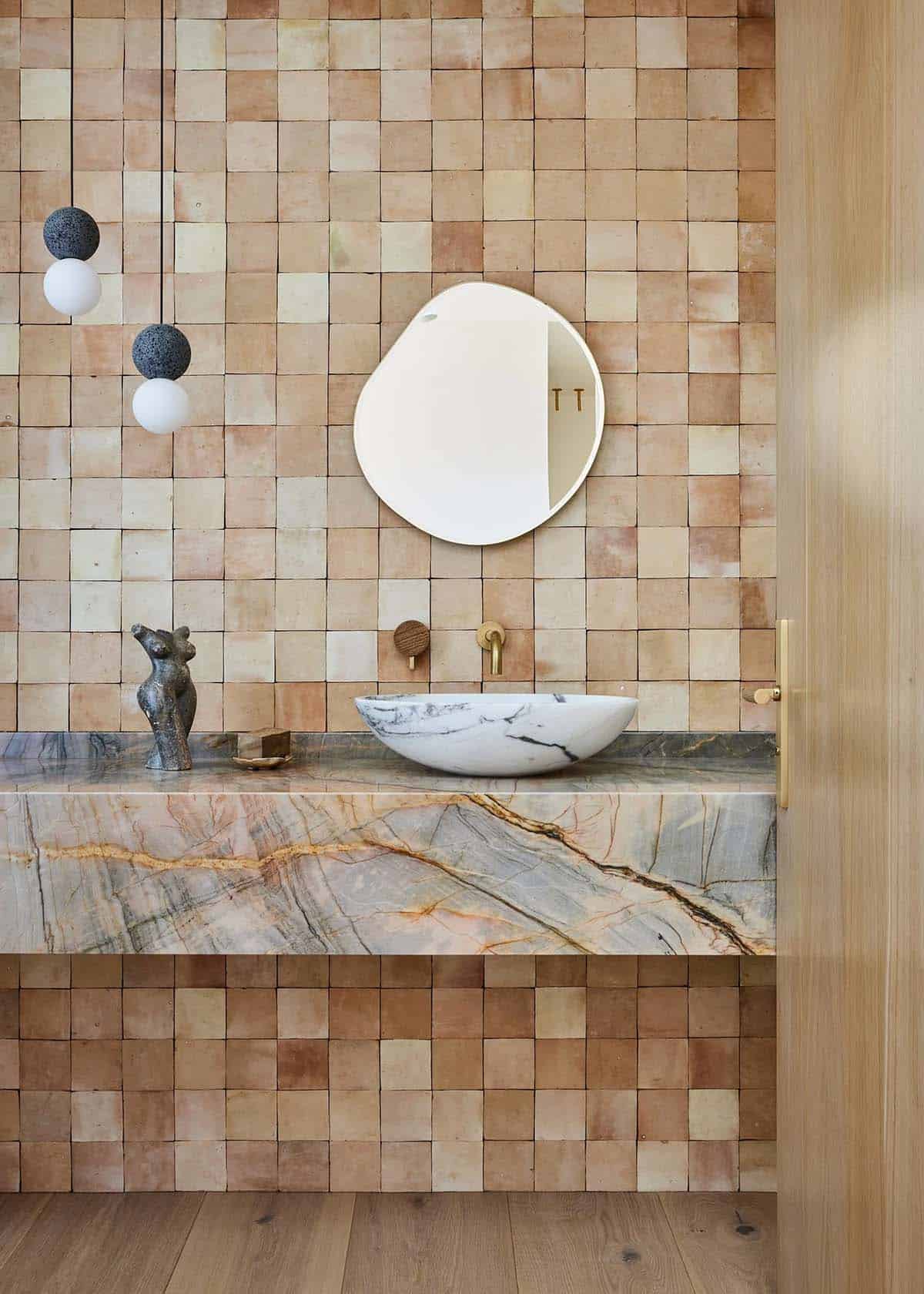 Powder room with handmade terracotta zellige tile walls, floating marble vanity shelf, vessel sink, organic mirror, and brass fixtures