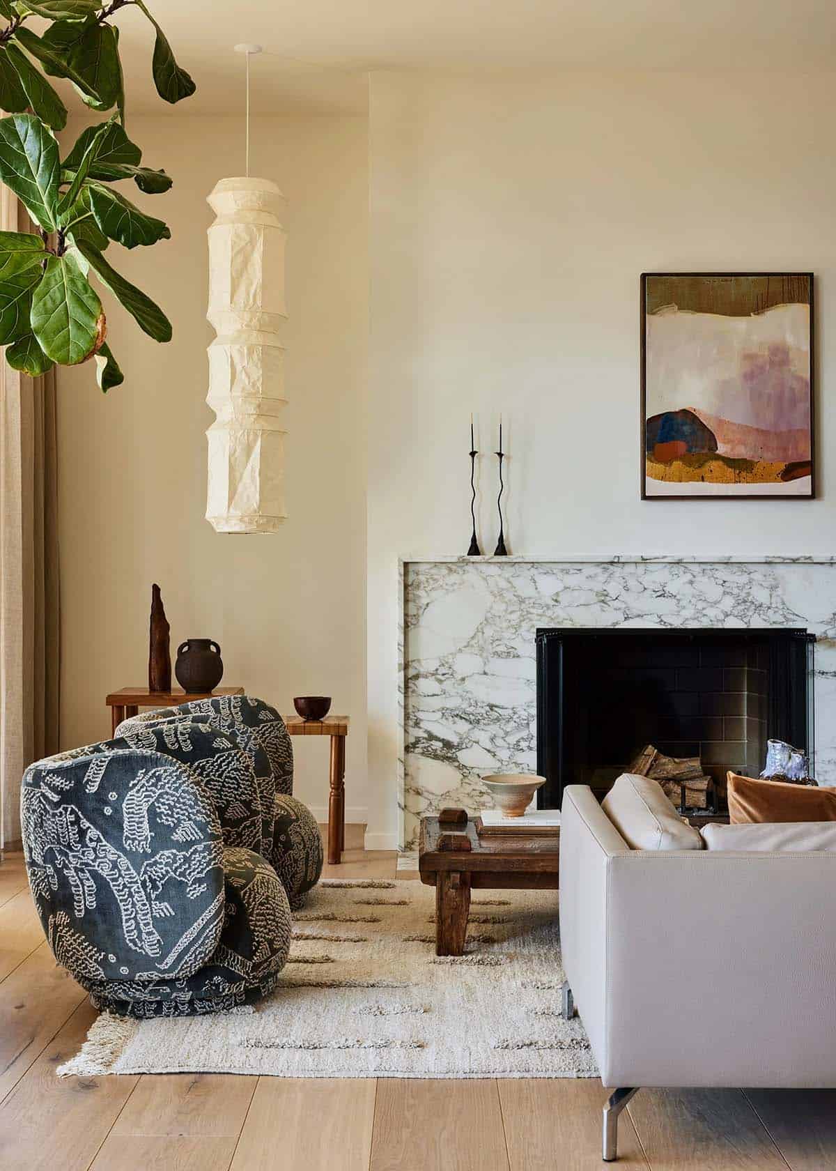 Living room corner with marble fireplace surround, sculptural patterned armchair, paper lantern pendant, and abstract landscape painting