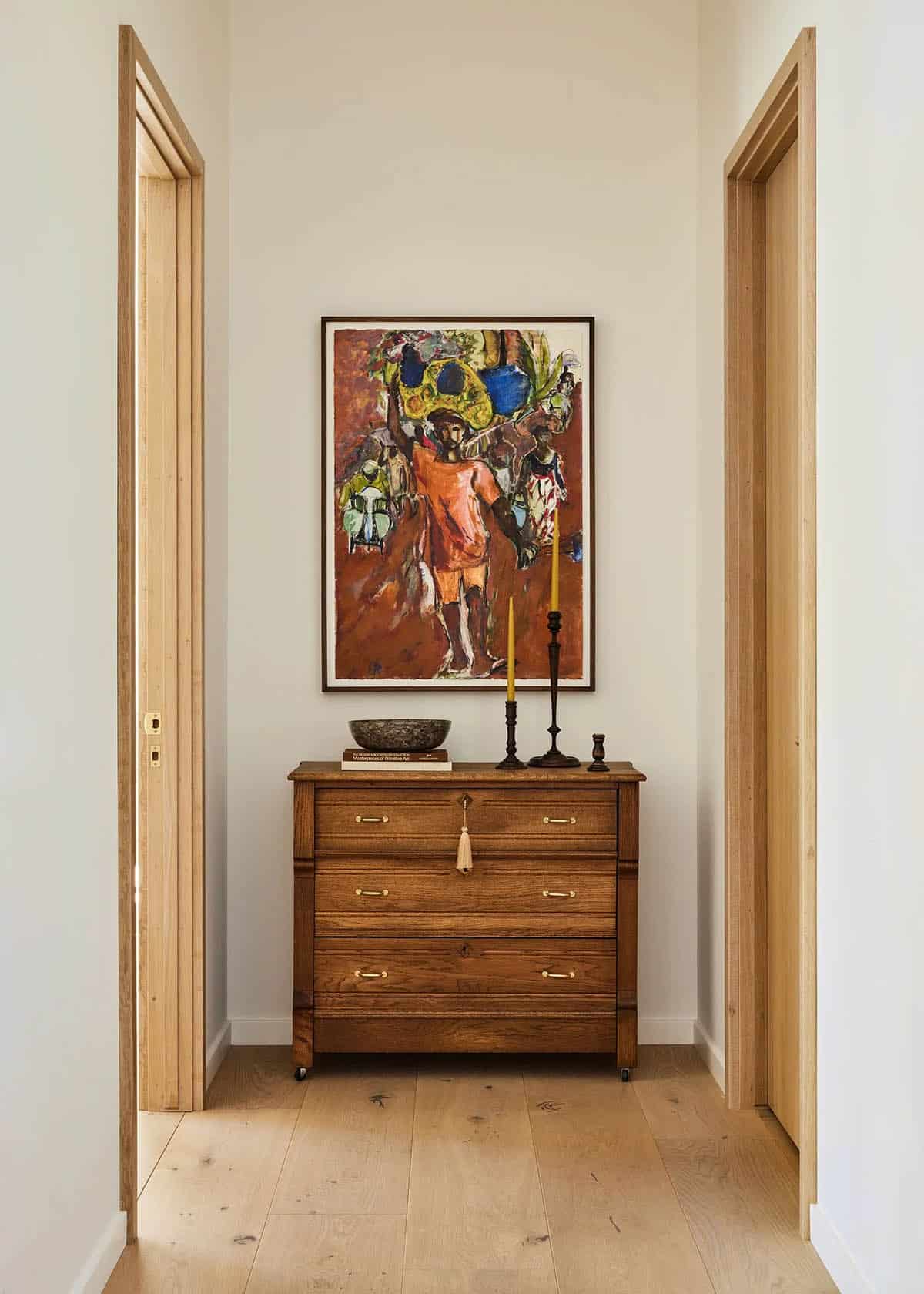 Hallway niche with antique oak dresser, colorful figurative painting, yellow taper candle, and light wood door frames