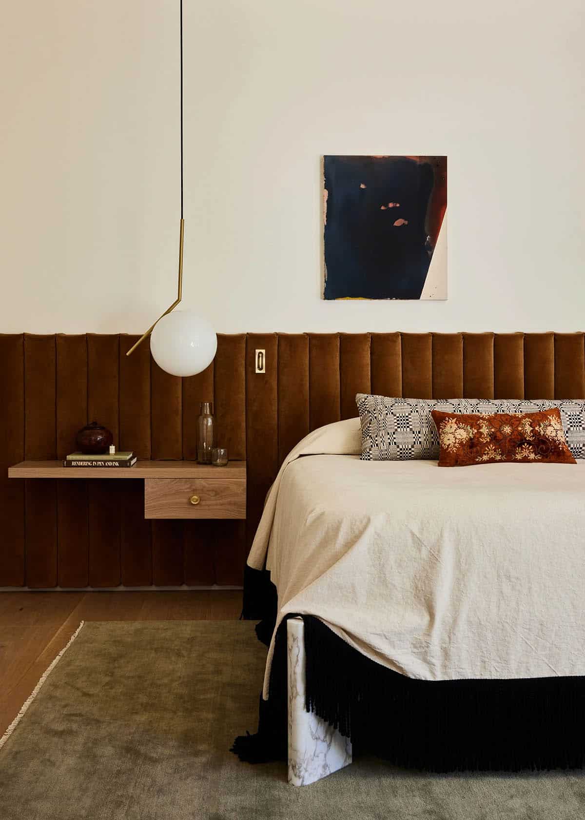 Primary bedroom detail showing channel-tufted velvet headboard, floating oak nightstand, globe pendant light, and small abstract artwork