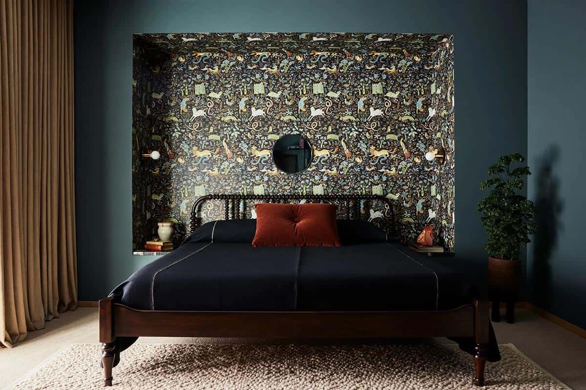 Guest bedroom with dark teal walls, dramatic animal-print wallpapered alcove framing the bed, dark navy bedding, and a round black mirror