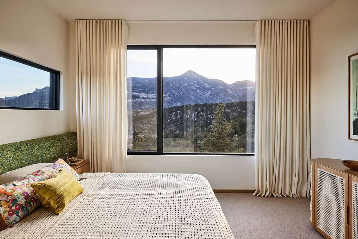 Guest bedroom with green floral upholstered headboard, colorful pillows, white waffle bedspread, and large picture window framing a mountain panorama