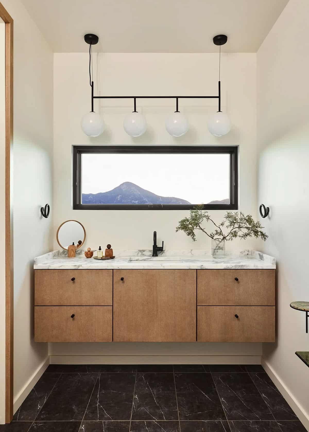 Guest bathroom with floating oak vanity, marble countertop, matte black faucet and knobs, four-globe black pendant bar, and narrow mountain-view window
