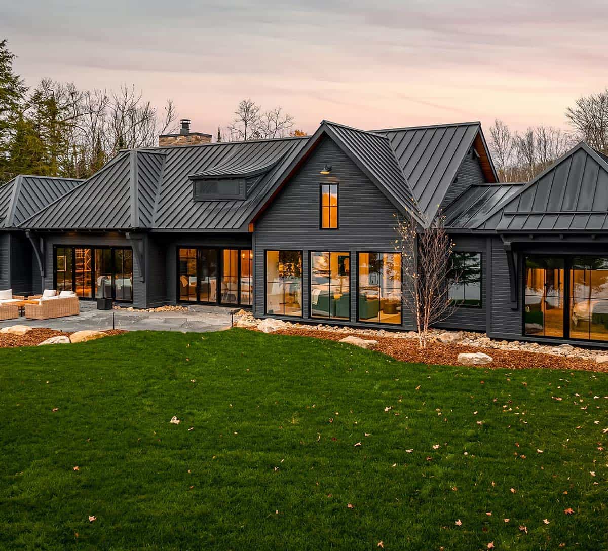 Dark gray modern farmhouse cottage with black metal roof and large windows at dusk, Ontario lakeside