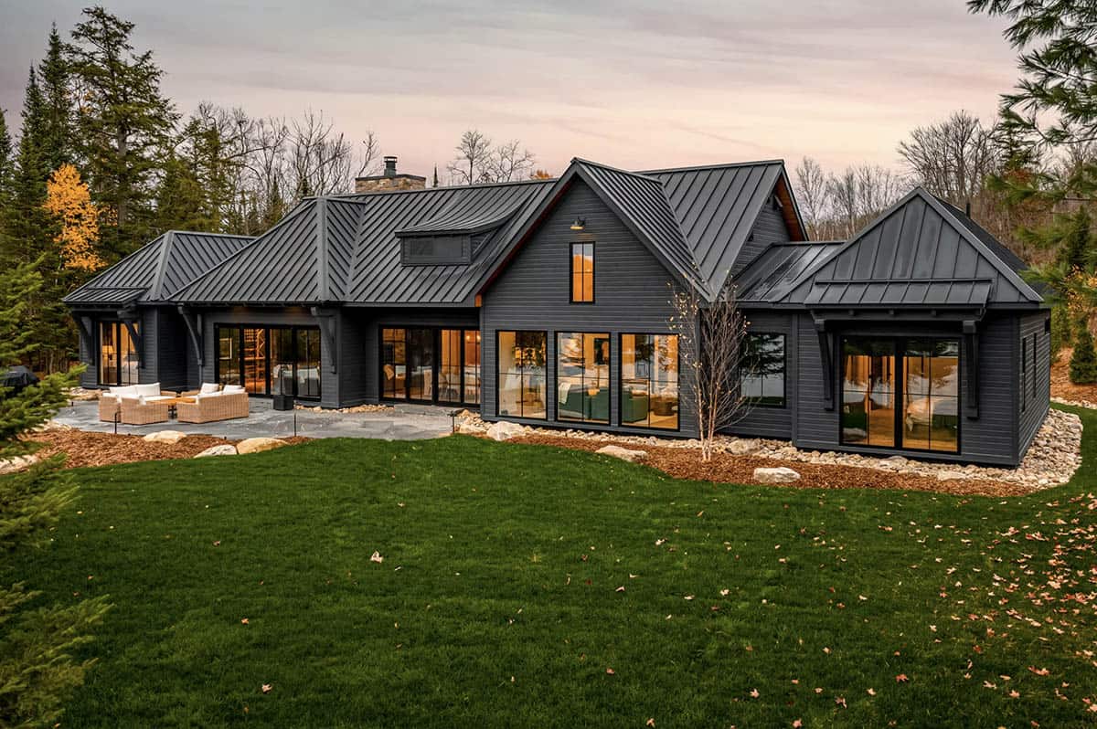 Front entrance of black modern cottage with oval door detail and gabled roofline, fall landscape