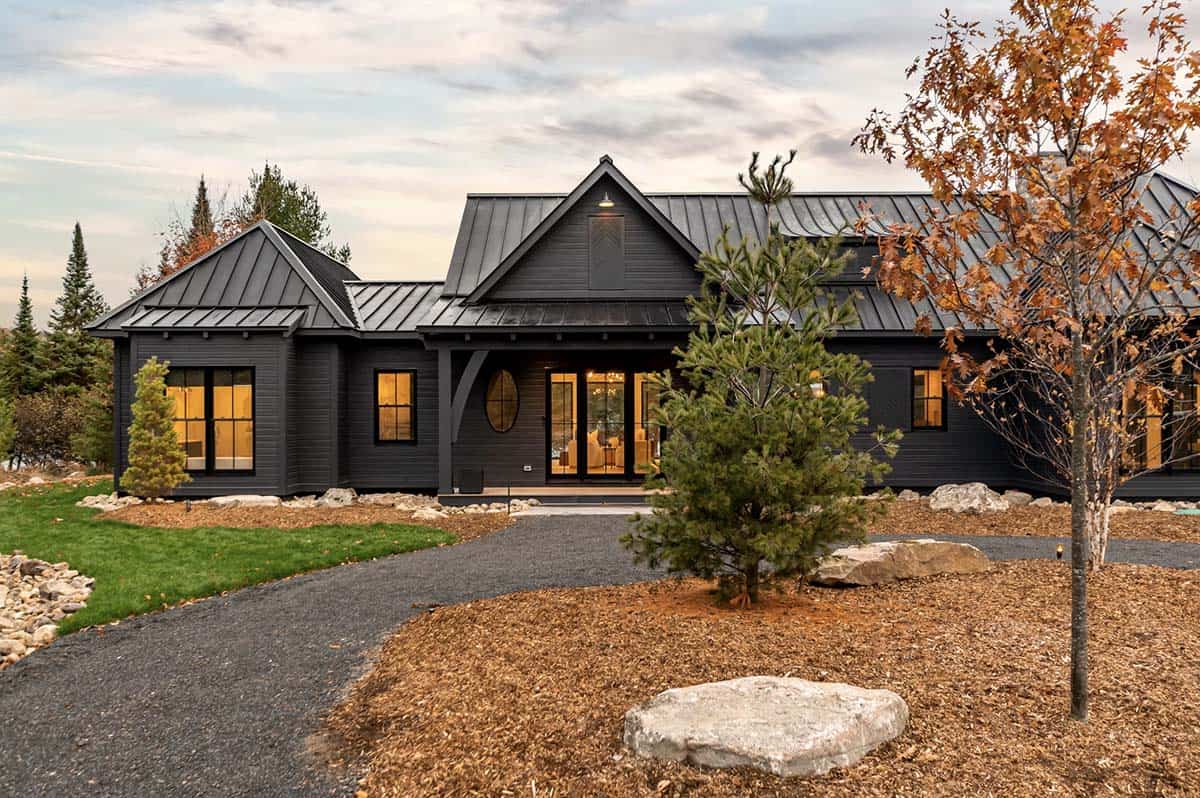 Aerial view of dark modern lakeside cottage with circular driveway and detached garage, autumn foliage