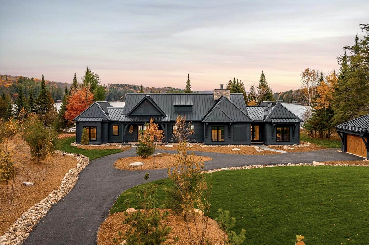 Bird's eye aerial of black cottage on lakefront property with wooden dock and fall forest
