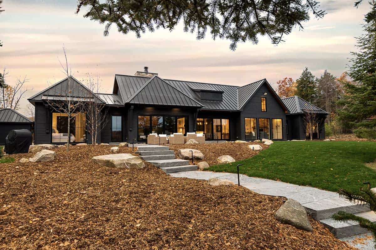 Wide aerial view of black cottage nestled on lakeside peninsula surrounded by fall foliage