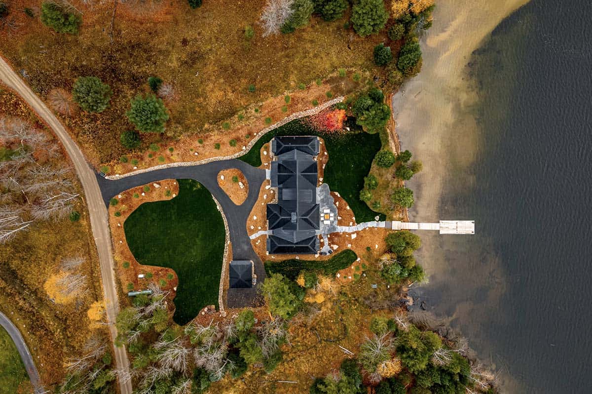 Angled aerial of lakeside black cottage with stone patio and wooden dock in autumn