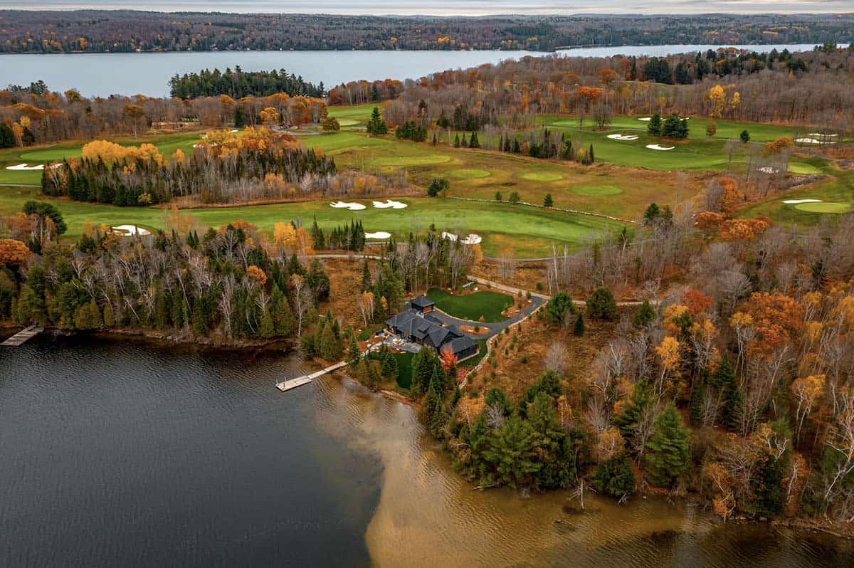 Water-level aerial of dark lakeside cottage with dock, golf course visible in background