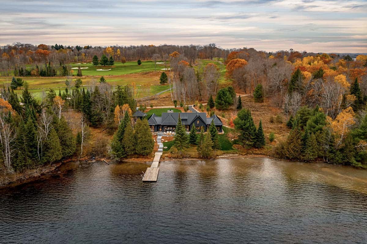 Long driveway approach to black modern cottage with detached garage, fall trees