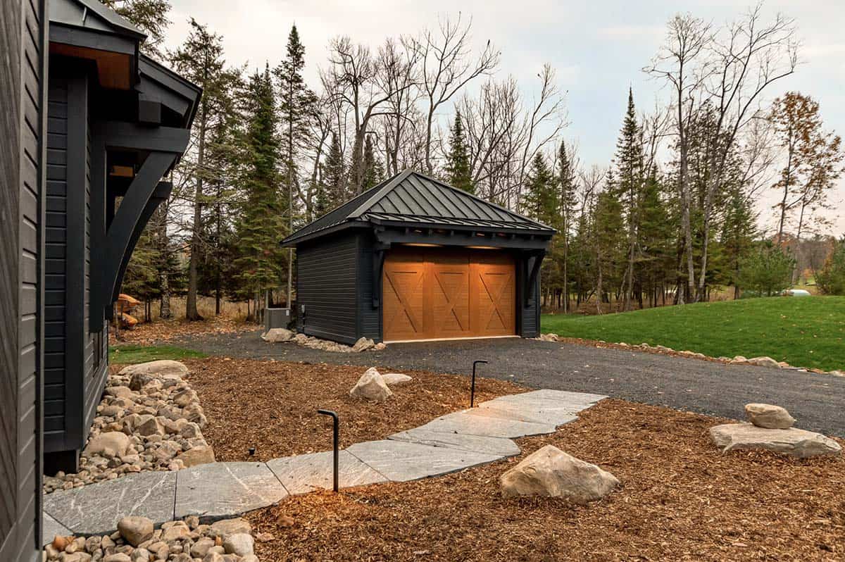 View of detached garage with cedar doors from main cottage entry with stone pathway