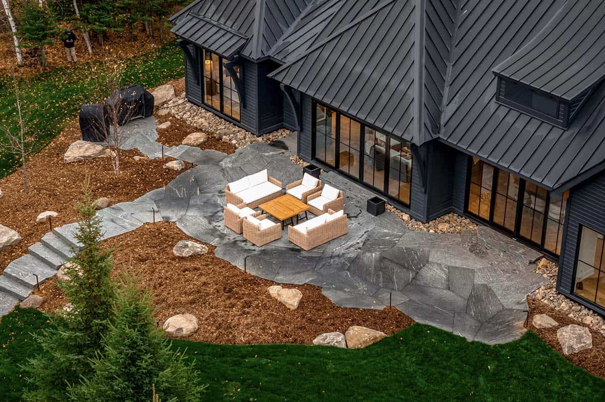 Close aerial of natural slate patio with wicker outdoor furniture beside cottage glass walls