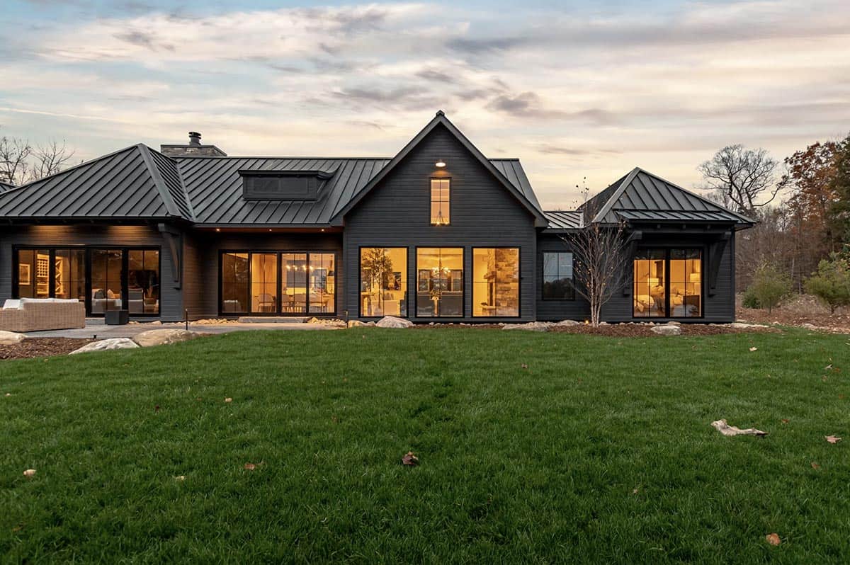 Glowing lakeside cottage rear facade at dusk with floor-to-ceiling windows and manicured lawn