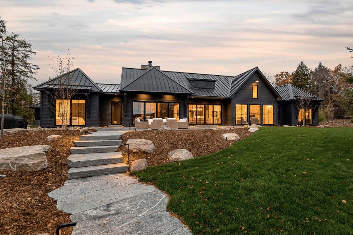Dark modern cottage rear exterior lit at twilight with stone pathway steps leading to patio