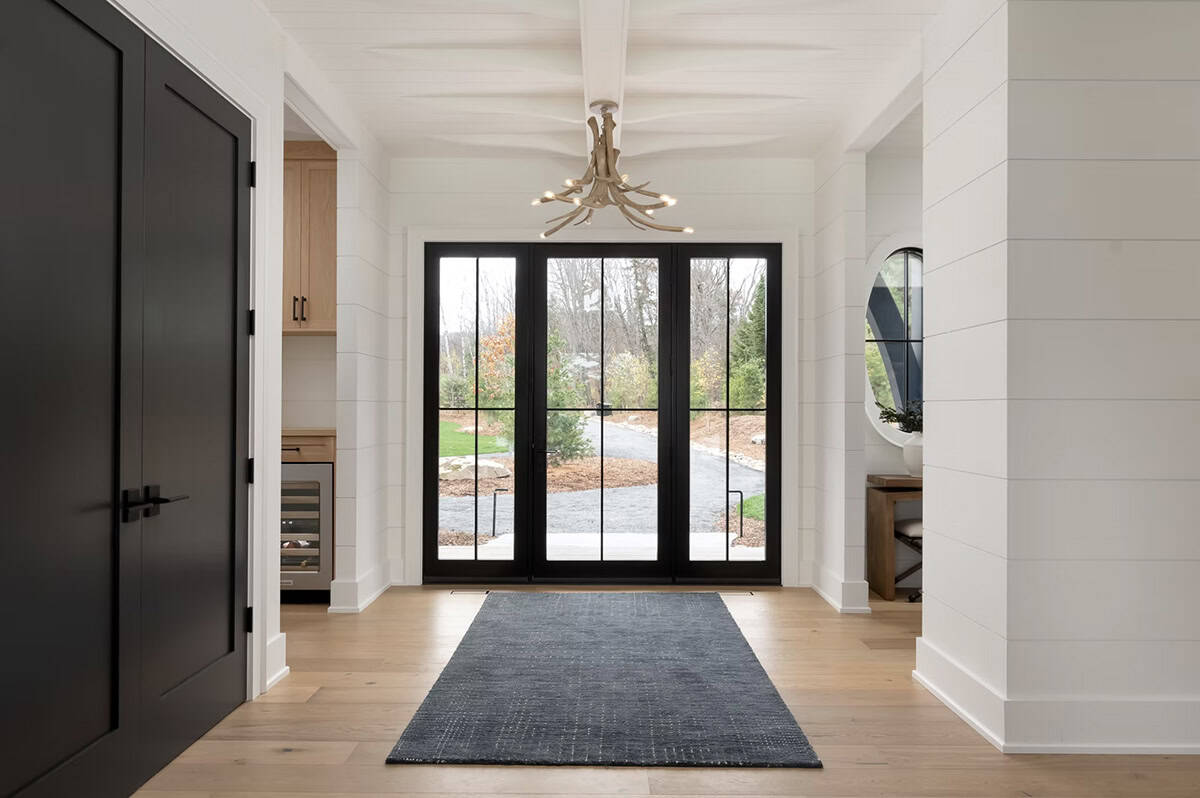 Bright cottage foyer with black French doors, antler chandelier, shiplap walls, and oak floors