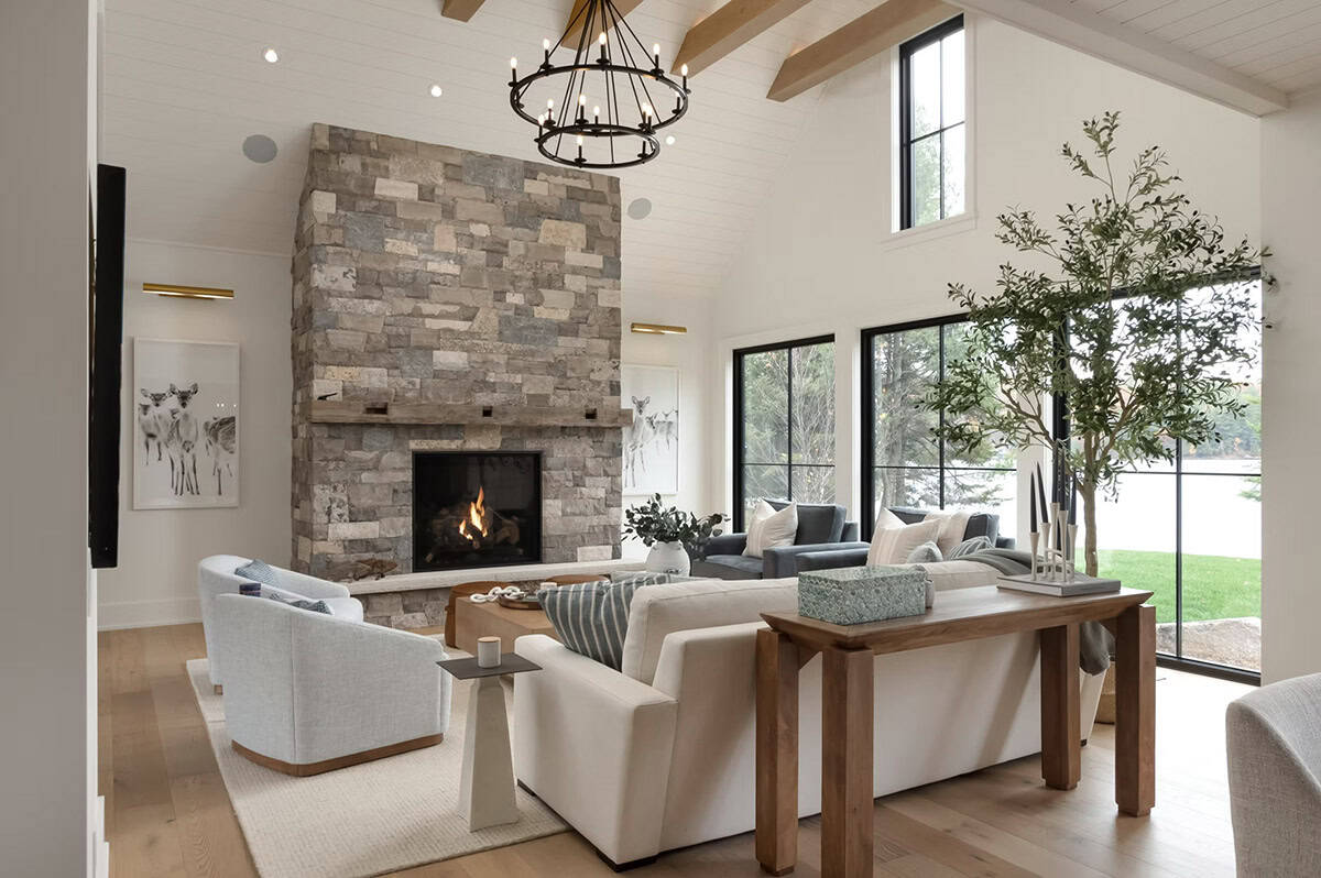 Bright cottage living room with stone fireplace, round chandelier, exposed beams, and large indoor tree