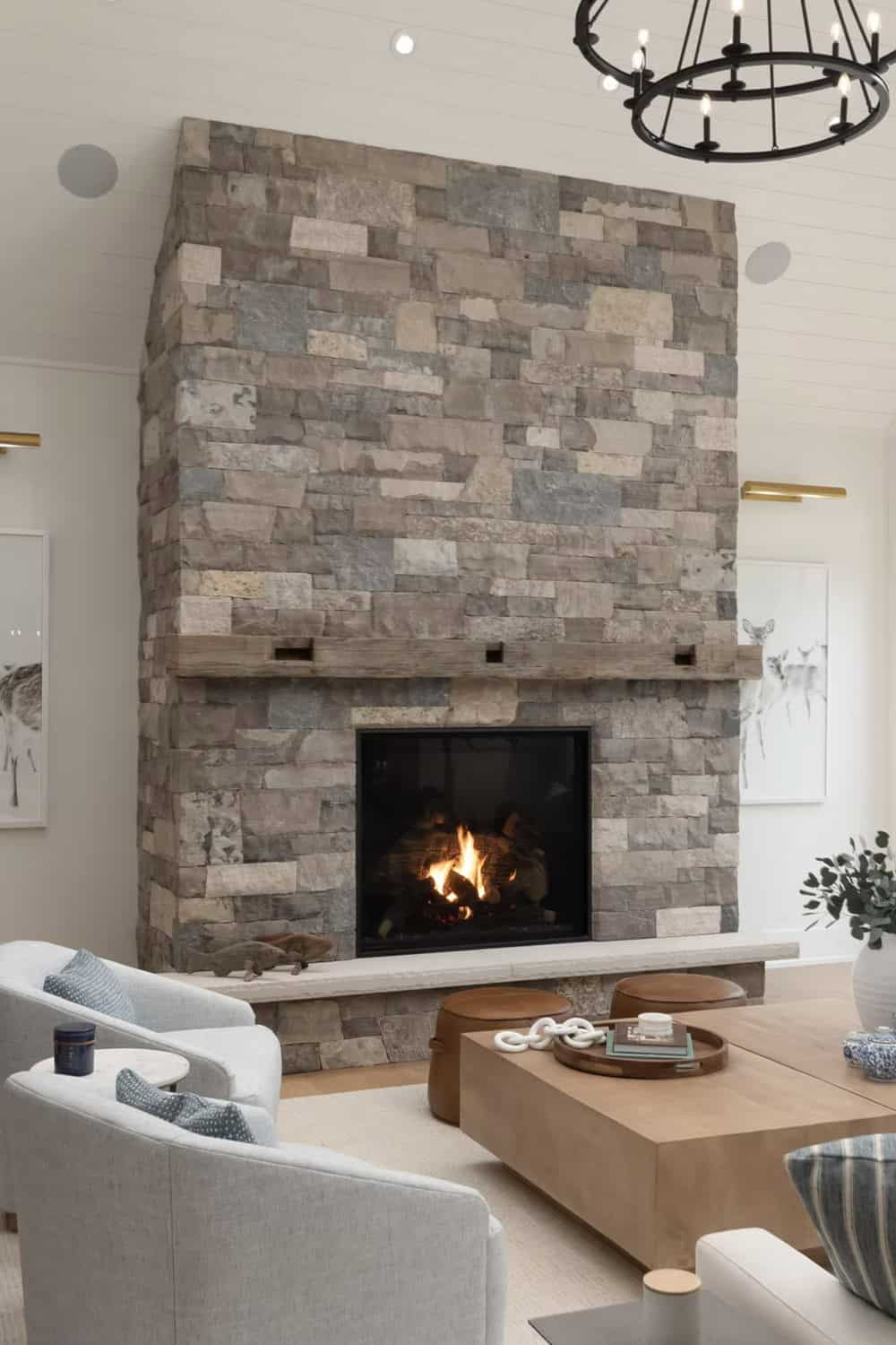 Close-up of stacked stone fireplace with wood mantel, lit fire, and black iron chandelier
