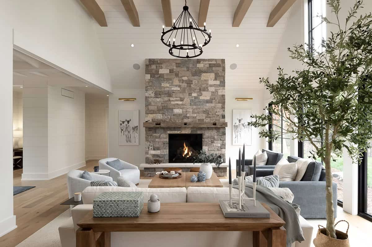 Open-concept living room with stone fireplace, vaulted beamed ceiling, olive tree, and lake views