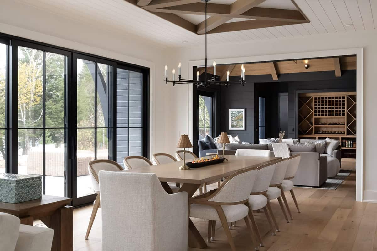 Dining area with geometric wood beam ceiling detail, long table, and view into dark-walled lounge and wine storage