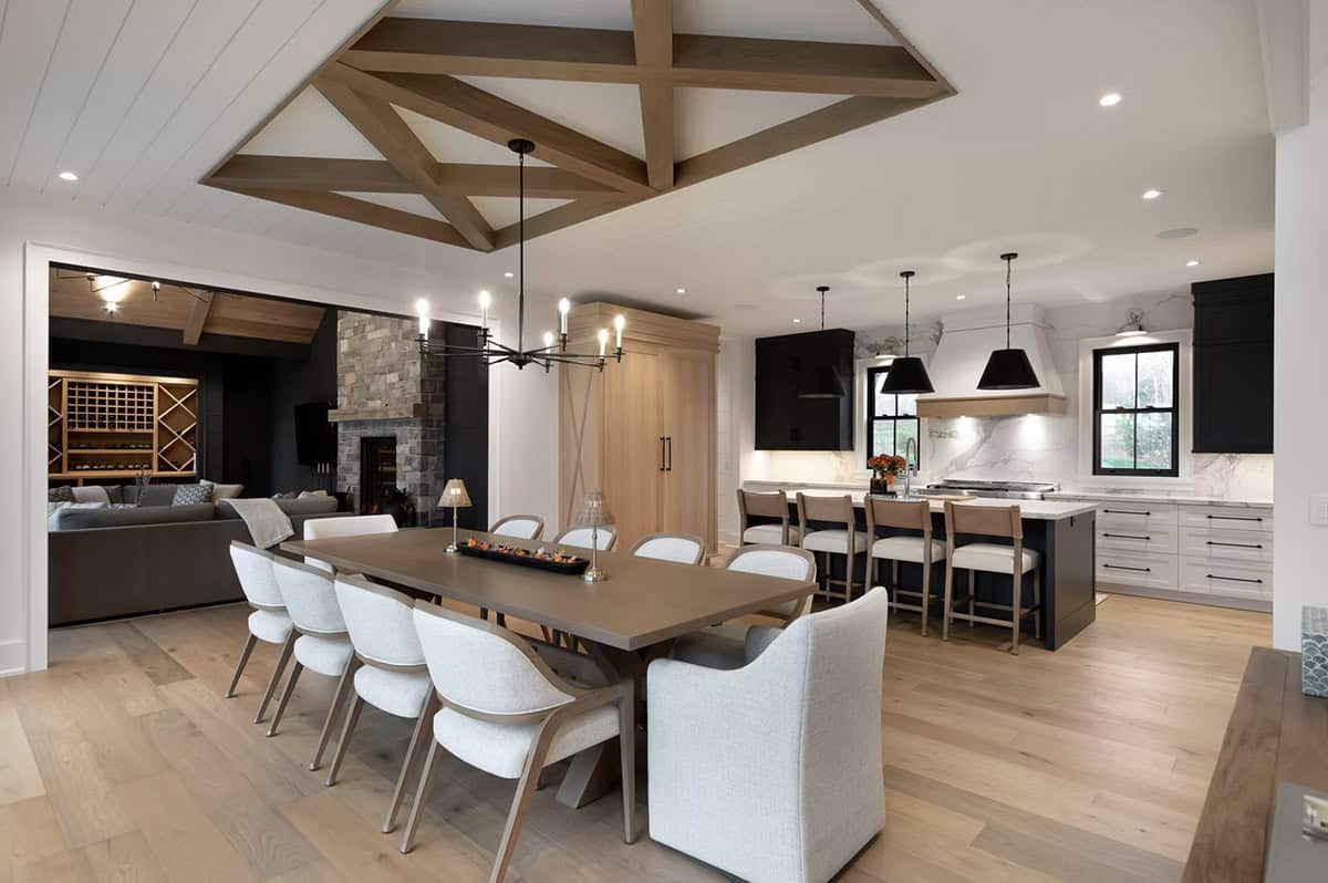 Open-plan dining and kitchen with geometric beam ceiling, long table, black cabinetry, and marble backsplash