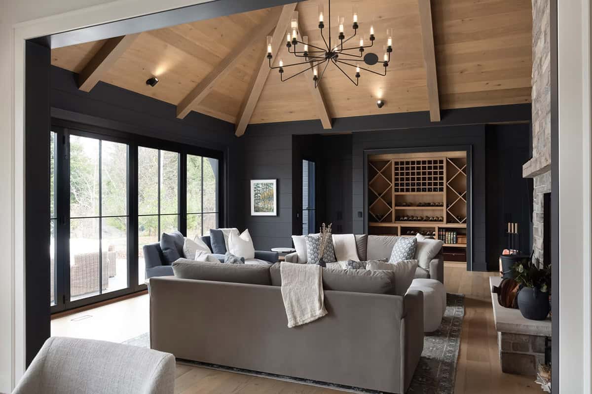 Dark-walled lounge with vaulted cedar ceiling, exposed beams, stone fireplace, and built-in wine storage