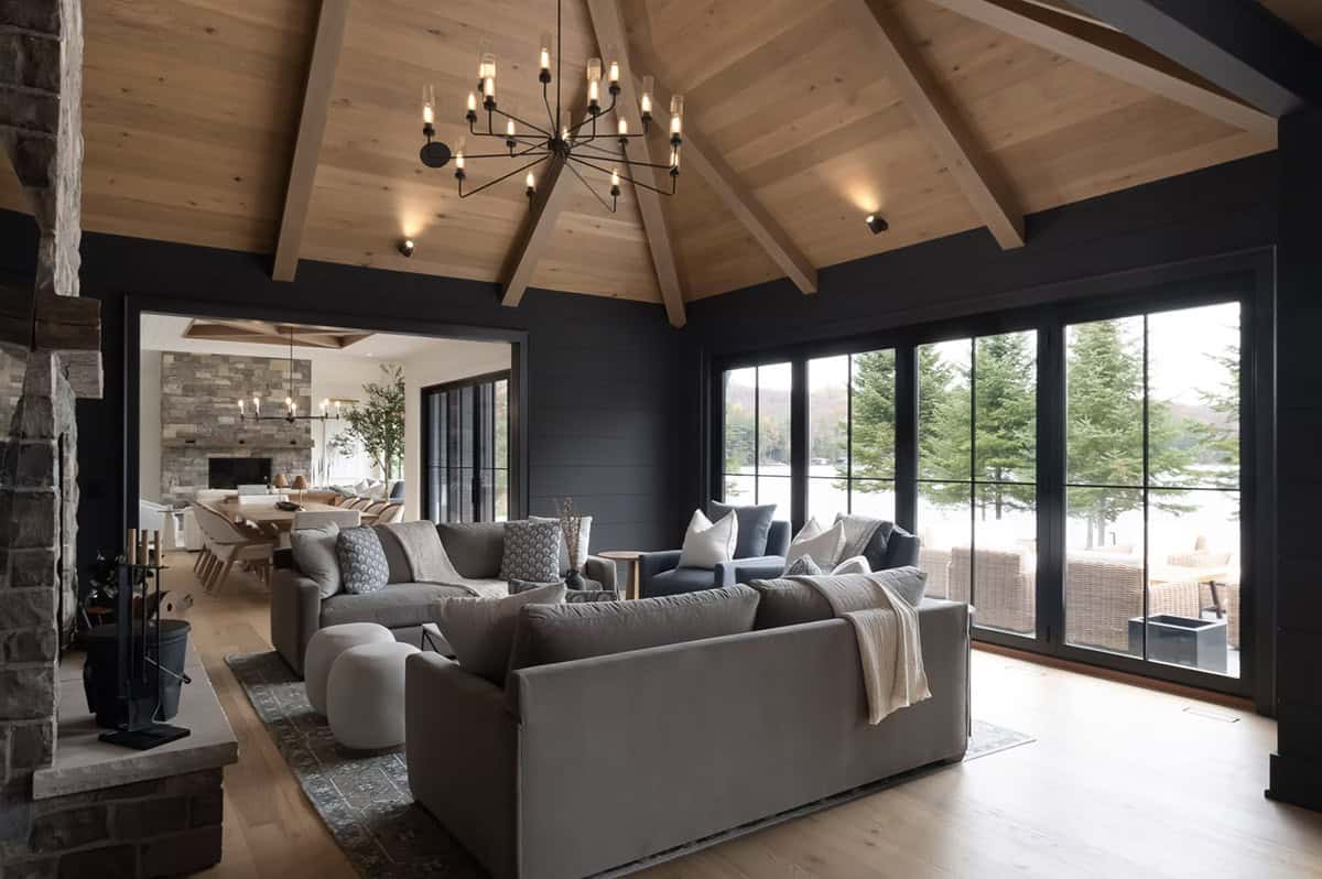 Dark-toned family lounge with cedar vaulted ceiling, stone fireplace, and floor-to-ceiling lake-view windows