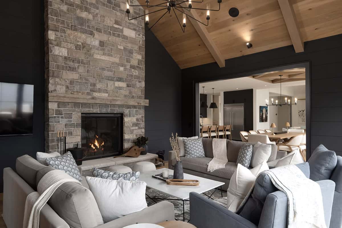 Dark-walled family lounge with floor-to-ceiling stone fireplace, cedar ceiling, and open view to dining area