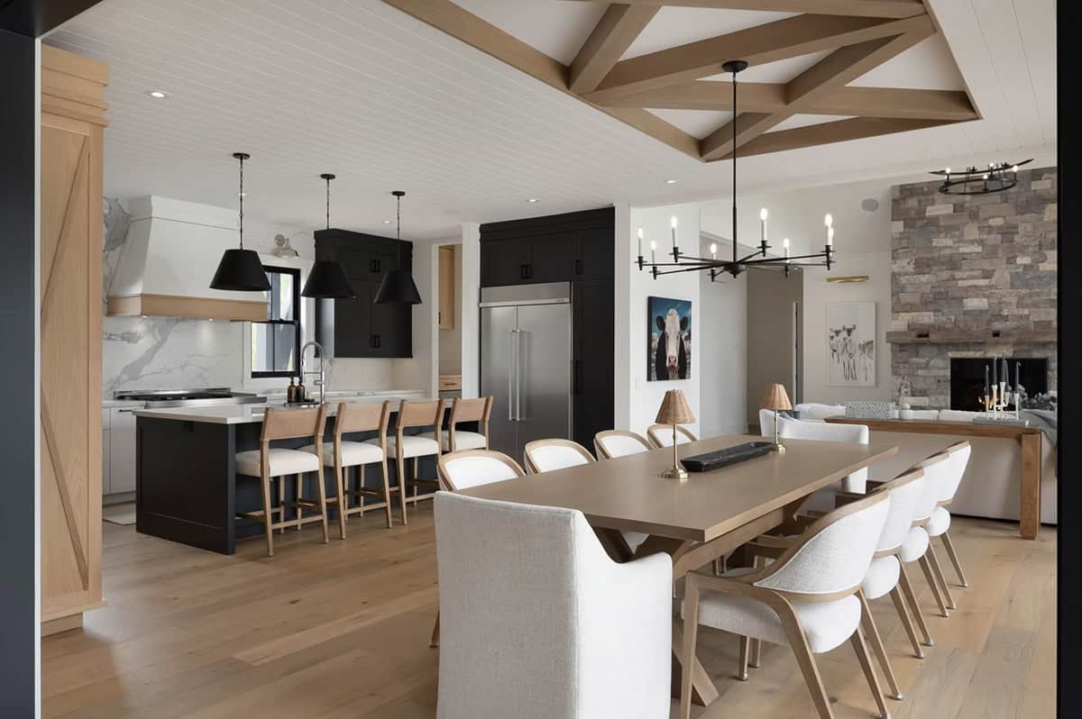 Open dining area with geometric beam ceiling connecting to black and white kitchen with marble backsplash