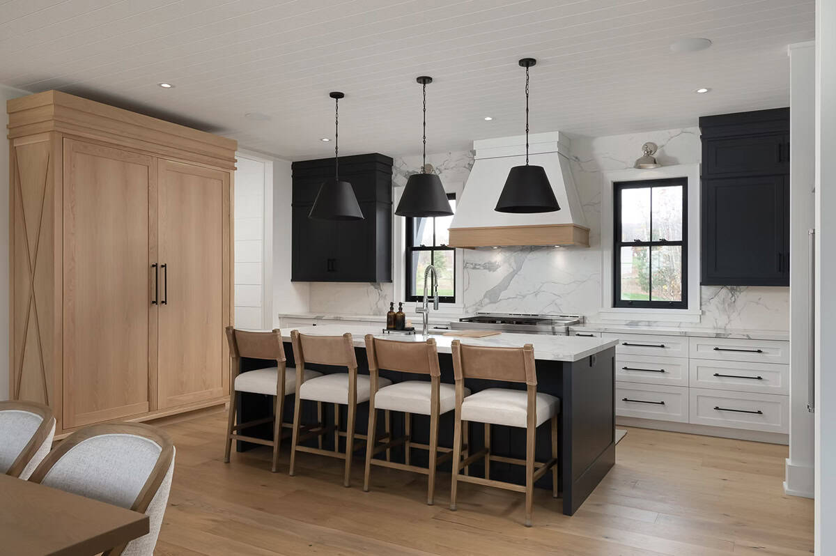 Cottage kitchen with black island, white cabinetry, marble slab backsplash, black pendant lights, and wood range hood