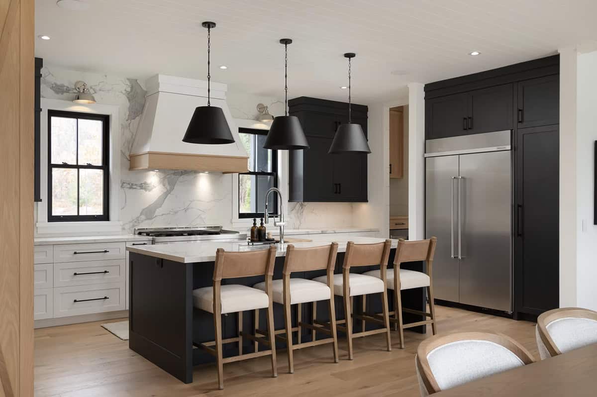 Cottage kitchen with black island, wood barstools, white range hood, marble backsplash, and stainless fridge