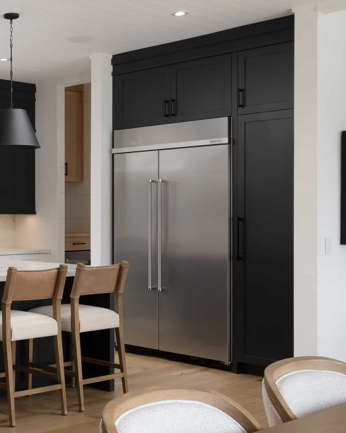 Built-in stainless side-by-side refrigerator flanked by dark floor-to-ceiling cabinetry in cottage kitchen