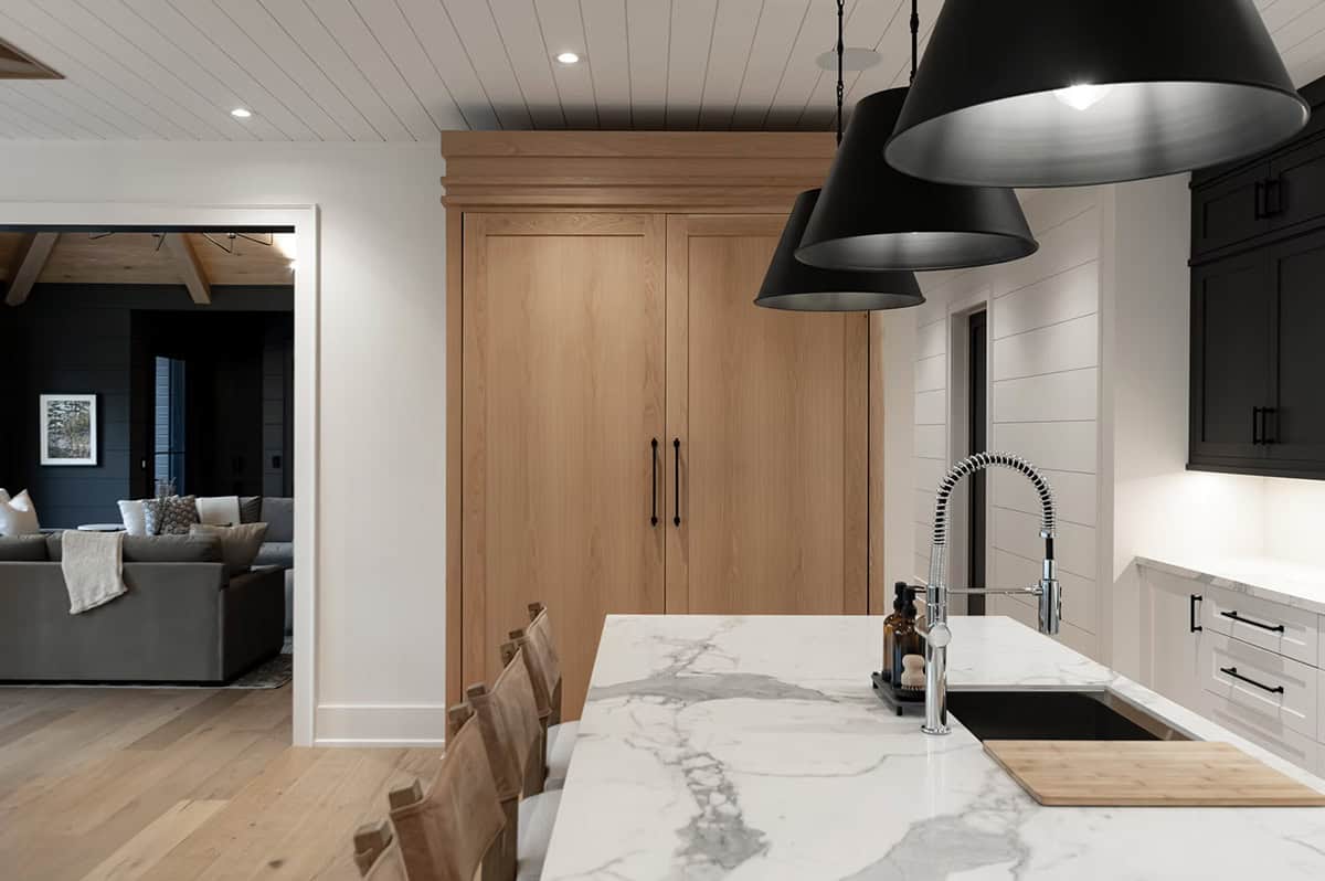 Kitchen island marble countertop with sink, wood pantry cabinet, and black pendant lights
