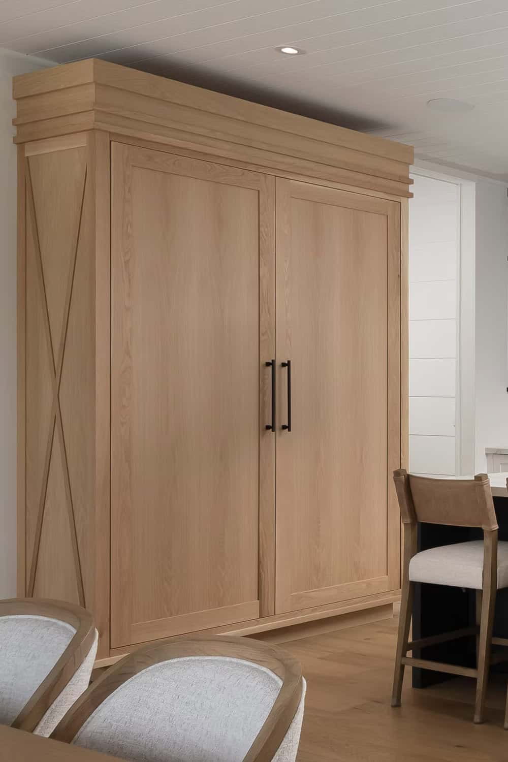 Tall custom natural oak pantry cabinet with X-detail and black hardware in cottage kitchen