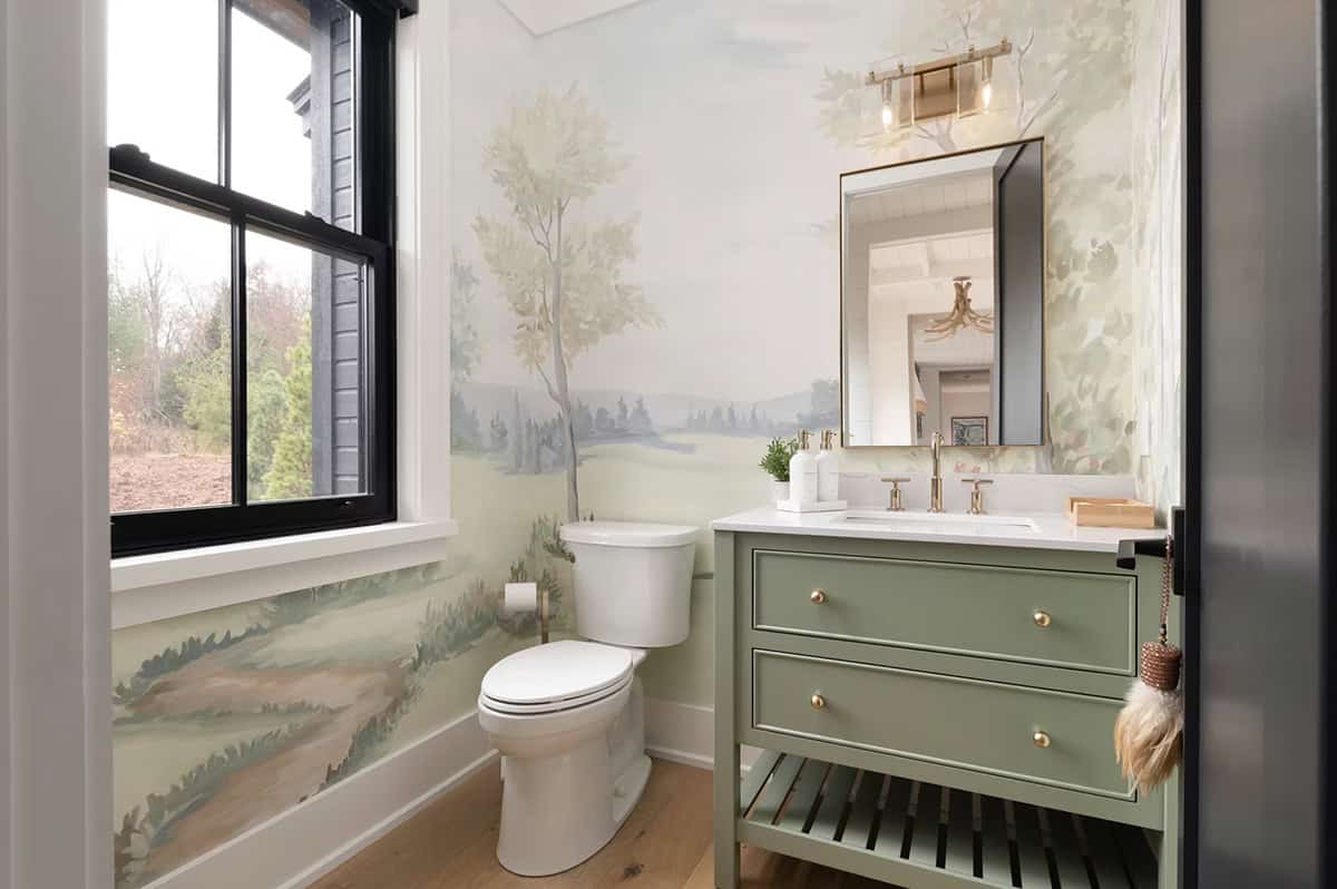 Full powder room view with sage green vanity, landscape mural wallpaper, black window, and brass fixtures