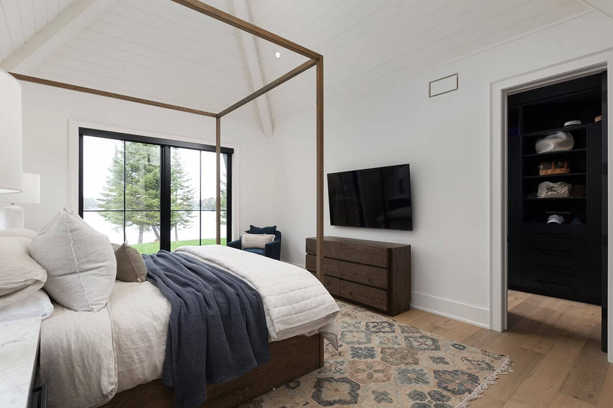 Primary bedroom with four-poster bed, lake view, wall-mounted TV, and glimpse into dark walk-in closet
