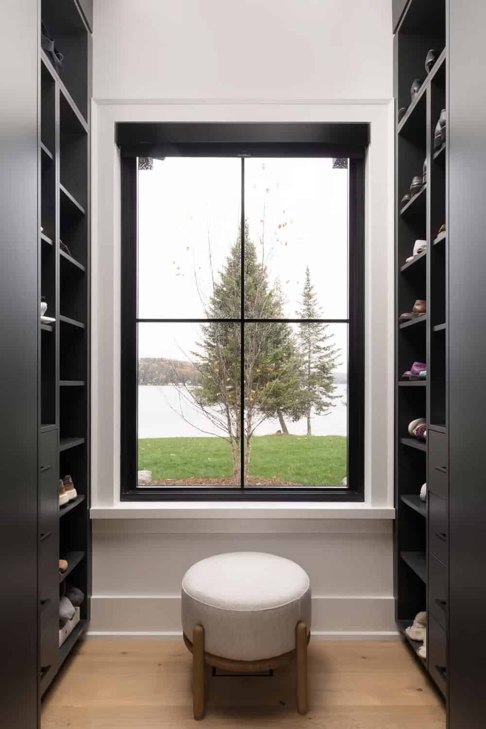 Walk-in closet open shoe shelves flanking black-framed lake view window with round upholstered stool
