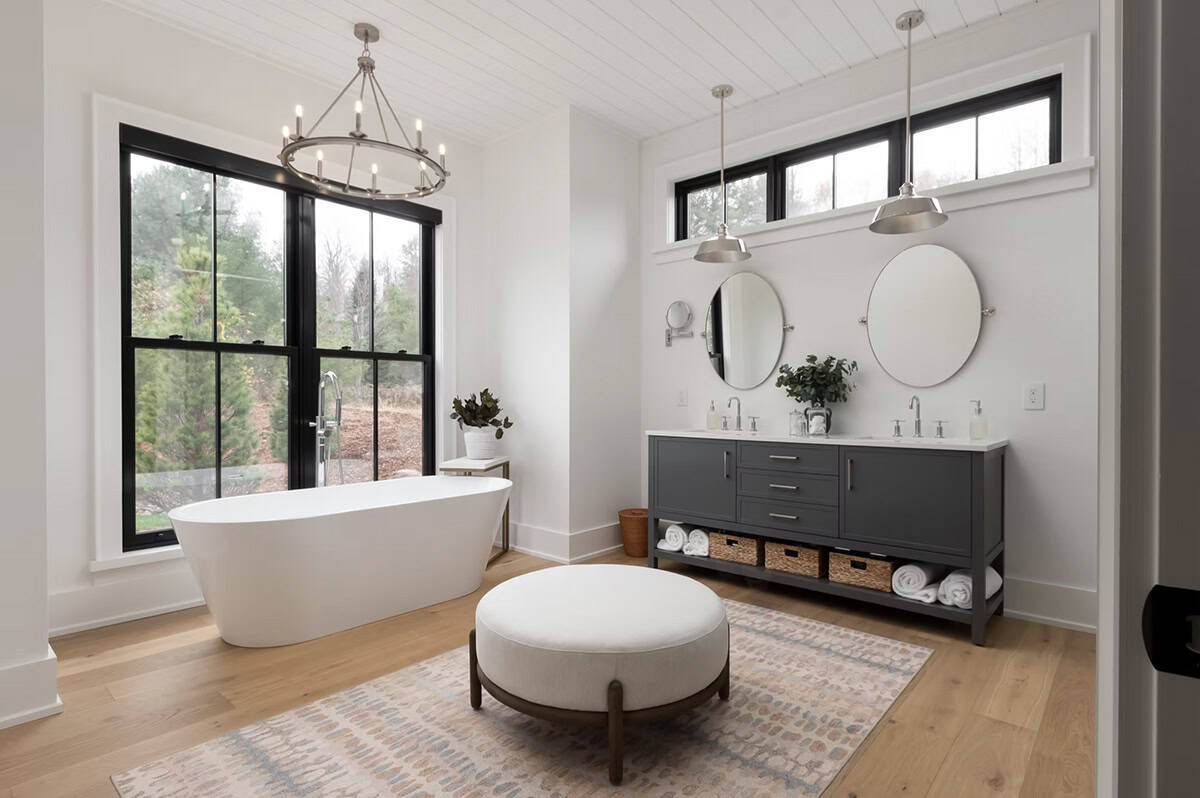 Primary ensuite with freestanding soaker tub, dark double vanity, oval mirrors, and large black-framed windows